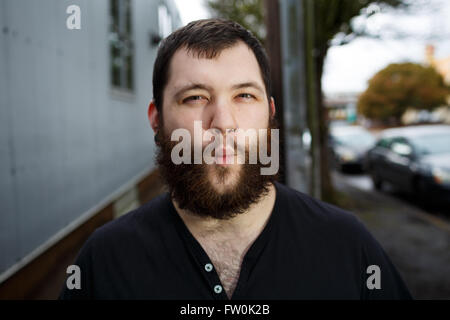 Junger Erwachsener Mann im Freien in einem städtischen Umfeld für Lifestyle Portrait eines bärtigen Hipster. Stockfoto