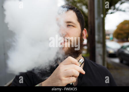 Urbaner Lifestyle Portrait von ein Mann Dampfen in einem städtischen Umfeld mit einem benutzerdefinierten Vape mod Gerät. Stockfoto