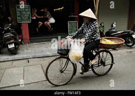 Touristen in ein Restaurant und eine Frau mit traditionellen konischen Hut mit ihrem Fahrrad in die alte Stadt von Hanoi, Vietnam Stockfoto