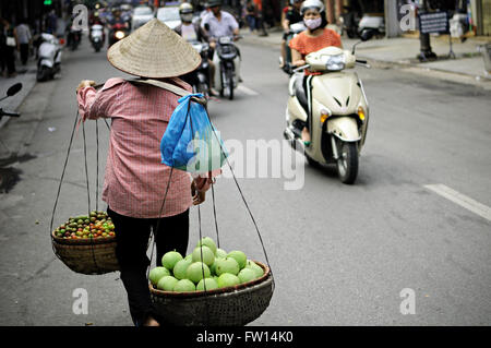 Frau Straßenhändler mit einem typischen kegelförmigen Hut zu Fuß in einer Straße von Hanoi, Vietnam Stockfoto