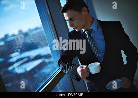Nachdenklich Geschäftsmann, trinken Kaffee und Blick durch die Fenster im Büro Stockfoto