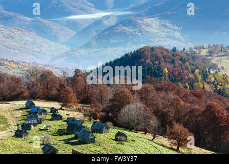 Morgennebel im Herbst Karpaten und hölzernen Scheunen am Hang. Stockfoto