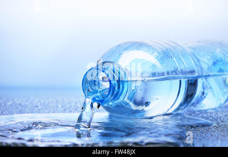 Wasser aus Kunststoff-Flasche mit Reflexion über weiß-blauen Hintergrund gießen Stockfoto