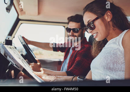 Seitenansicht des jungen Paares Lesen einer Karte nach dem Weg. Junger Mann und Frau im Auto los Roadtrip. Stockfoto