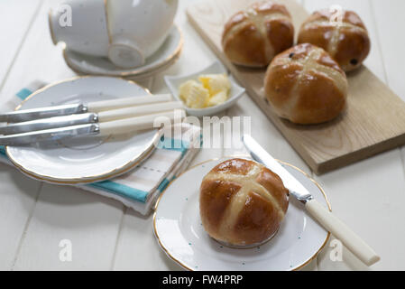 Hausgemachte Hot Cross Buns auf einer Creme lackiert Tischset mit feinstem Porzellanteller und Tassen. Stockfoto