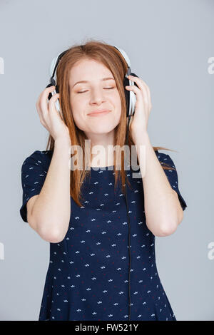 Glückliche Frau hören von Musik im Kopfhörer über grauen Hintergrund Stockfoto