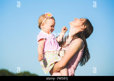 Mutter mit ihrem Kind außerhalb an sonnigen warmen Tag spielen. Porträt von glücklich lachende Frau und kleines Mädchen am blauen Himmelshintergrund Stockfoto