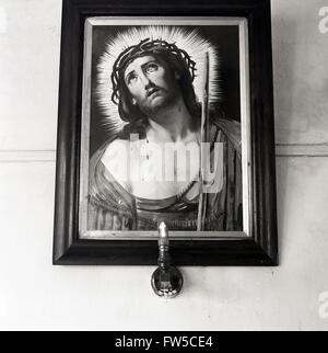 1950er Jahre historische, gerahmte Gemälde von Jesus Christus an Wand mit Licht darunter Irland, zeigt einen Ring aus Licht oder Halo allgemein verwendet in der Kunst als Symbol für das Licht der Gnade von Gott verliehen. Stockfoto