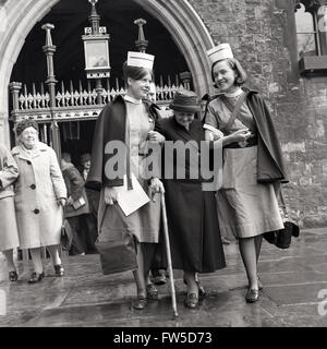 historische, der 1950er Jahre helfen zwei weiblichen Krankenschwestern eine ältere Dame vor Westminster Abbey, London, nach Erhalt "Maundy Money", eine besondere Gabe von der Königin an die 40 Rentner in Anerkennung Service für ihre Gemeinde oder Kirche.      Die Royal Maundy Service Swan Upping Zustand besucht Stockfoto