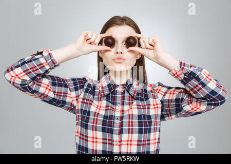 Schöne lustiger Teenager-Mädchen im karierten Hemd bedeckt ihre Augen mit runden Pralinen Stockfoto