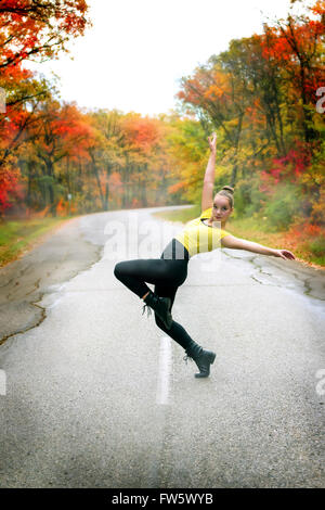 Ein junges Mädchen tanzt draußen auf der Straße im Herbst Stockfoto
