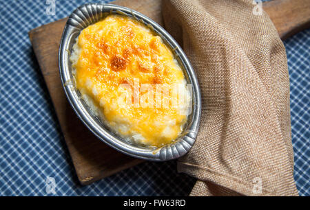 Overhead shot von hominy Grits gebacken mit Cheddar Käse in eine kleine antike Zinn Schüssel servieren. Stockfoto