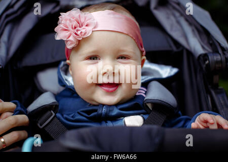 Babysitter in einen Kinderwagen, mit meiner Mutter Finger, eine Bandage auf dem Kopf mit einer rosa Blume. Baby lächelt und auf der Suche Stockfoto