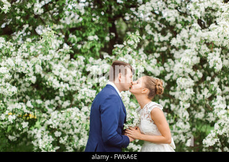 elegante stilvolle Bräutigam mit seiner glücklich wunderschöne Brünette Braut auf dem Hintergrund der Apfelbäume im park