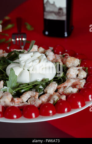 Salat Käse Buratti, Garnelen, Rucola, Cherry-Tomaten mit Olivenöl, serviert auf einem roten Hintergrund mit einer Gabel, Nahaufnahme Stockfoto