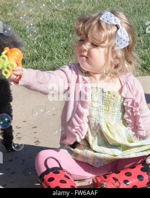 Ein zwei Jahres altes kaukasischen Kleinkind Mädchen macht Seifenblasen mit einem Spielzeug-Bubble-Maker. Stockfoto