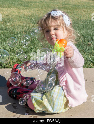 Ein zwei Jahres altes kaukasischen Kleinkind Mädchen macht Seifenblasen mit einem Spielzeug-Bubble-Maker. Stockfoto