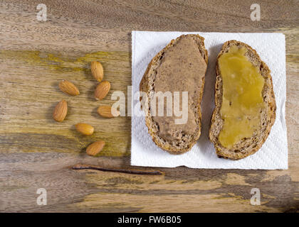 Roggenbrot mit Mandelbutter und rohen kristallisierten Honig für leckere gesunde Sandwich auf Alter Holzbrett garniert Stockfoto