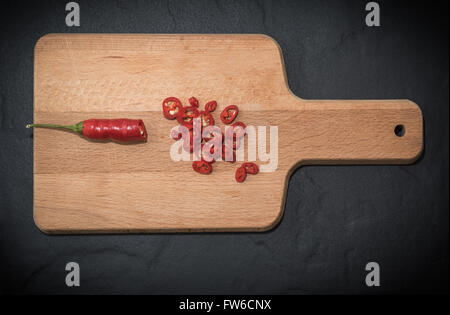 Rustikale Schneidbrett aus Holz auf einem schwarzen Schiefer Hintergrund rote Chilischoten gehackt Textfreiraum Stockfoto