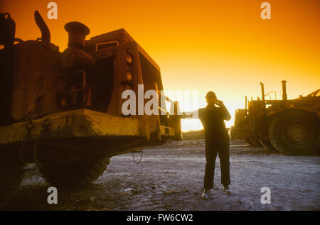 Bauarbeiter sprechen auf einem Handy neben einem Bagger bei Sonnenuntergang Stockfoto