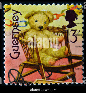 GUERNSEY - CIRCA 1994: Eine Briefmarke gedruckt in Guernsey gewidmet vergangener Spielzeug zeigt Teddybär auf einem Stuhl, ca. 1994 Stockfoto