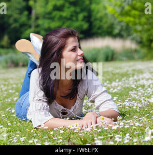 Hübsche junge Frau mit dunklen langen Haaren liegen auf dem Rasen in einem park Stockfoto