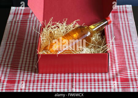 Rote Box gefüllt mit Stroh und einer Flasche, stehend auf einer aufgegebenen Tischdecke. Stockfoto