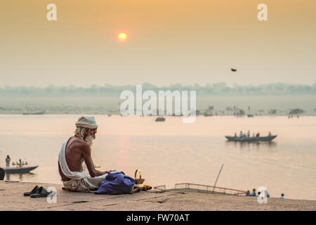 Ein Sadhu (hinduistischen frommen eifrigen Anhänger) sitzt am heiligen Fluss Ganges in Varanasi, im Hintergrund die Sonne aufgeht. Stockfoto