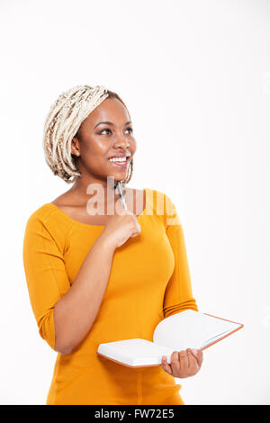 Glücklich attraktive junge afroamerikanische Frau lächelnd und schreiben in Notebook auf weißem Hintergrund Stockfoto