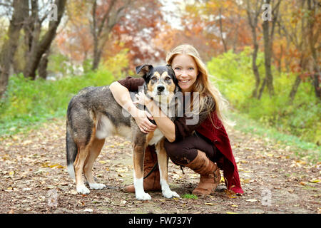 Eine 30 Jahre alte Frau hält um ihr Deutscher Schäferhund zu umarmen, wie sie durch das Laub in den Wäldern Fuß sind Stockfoto