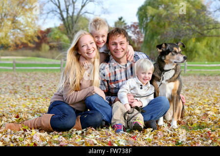 Eine glückliche Familie von vier Personen, darunter Mutter, Vater, Kind und Kleinkind Bruder sitzen draußen im Laub Stockfoto