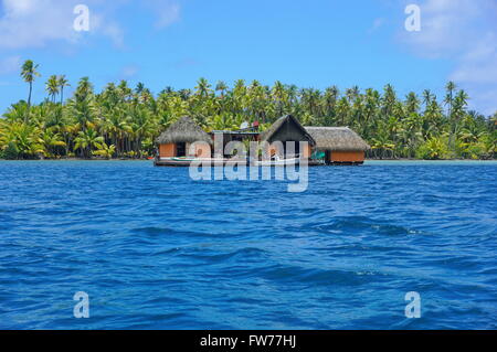 Exotische Haus mit Strohdach über dem Wasser und eine Plantage mit Kokosnuss-Palmen im Hintergrund, Huahine, Französisch-Polynesien Stockfoto