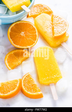 Hausgemachte, natürliche Orange, erfrischende Sommer Eis am Stiel. Von oben flach lag auf weißem Marmor mit frischen Orangenscheiben. Stockfoto