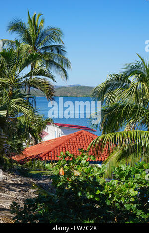 Zwischen tropischen Palmen und roten Dächern den Blick auf das kristallklare blaue Wasser Stockfoto