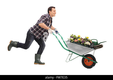 Junge fröhliche Gärtner Schubkarre voller Blumen und laufen isoliert auf weißem Hintergrund Stockfoto