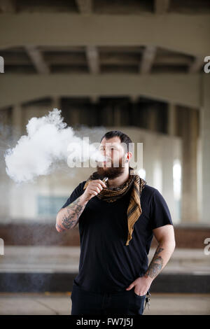 EUGENE, OR - 20. März 2016: Urban Porträt eines bärtigen Hipster mit Tätowierungen Dampfen mit einem benutzerdefinierten mod Vape-Gerät. Stockfoto