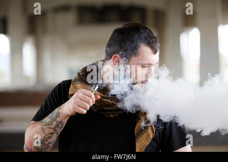 EUGENE, OR - 20. März 2016: Urban Porträt eines bärtigen Hipster mit Tätowierungen Dampfen mit einem benutzerdefinierten mod Vape-Gerät. Stockfoto