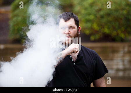 EUGENE, OR - 20. März 2016: Urban Porträt eines bärtigen Hipster mit Tätowierungen Dampfen mit einem benutzerdefinierten mod Vape-Gerät. Stockfoto