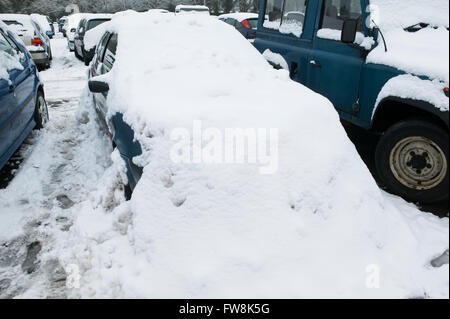 Geparkte Autos in einer dicken Schicht Schnee bedeckt, so dass sie nahezu unsichtbar sind speichern für Räder und Stoßstangen unter die gefrorene weiße Decke zeigt. Stockfoto
