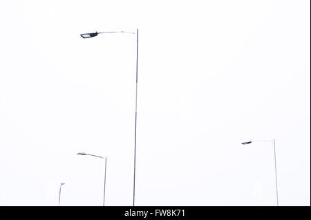 Straßenlaternen oder Laternenpfähle abgedeckt auf der einen Seite durch eine Schicht aus Schnee zeichnen sich gegen den Winter Himmel wie abstrakte Skulpturen zeigen als dünne Linien von weiß und schwarz. Stockfoto