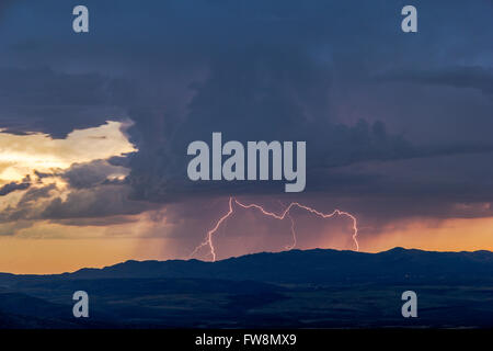 Entfernter Blitz von Wolke zu Boden über einem Berg während eines Gewitters bei Sonnenuntergang Stockfoto