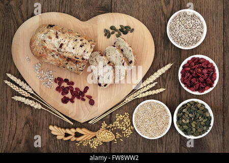 Cranberry Seed Brot auf Brett mit Weizen und Hüllen, Sonnenblumen und Kürbis-Samen, Haferflocken und getrocknete Cranberries in Herzform. Stockfoto