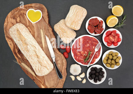 Antipasti mit Oliven, Salami, getrockneten und frischen Tomaten, Knoblauch, Zitrone, Öl, mit Ciabatta-Brot auf einem Oliven Holz Brett Stockfoto