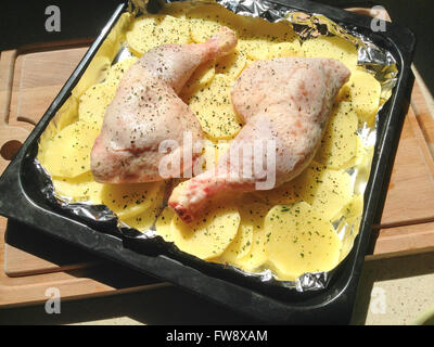 Roh marinierte Hähnchenschenkel mit Kartoffeln auf ein Backblech legen und Schneidebrett Stockfoto