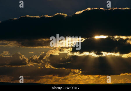 Einen dramatischen Sonnenuntergang die Sonne untergeht es glänzt durch Brüche in der niedrigen Wolken und sendet tief orange, gelb und rot Strahlen Shoting ausfüllen den Himmel. In dieser Szene sieht es fast apokalyptische oder möglicherweise geistige, als ob etwas großes passieren soll. Stockfoto