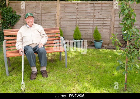 Porträt der ein älterer Mann sitzt in seinem Garten lächelnd Stockfoto