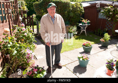 Älterer Mann mit einem Gehstock in seinem Garten lächelnd Stockfoto