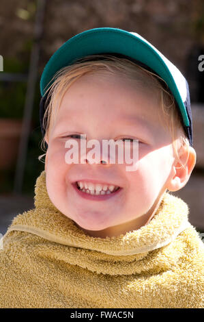 Porträt eines glücklich lächelnden kleinen Jungen eingewickelt in ein Handtuch mit einer Mütze Stockfoto