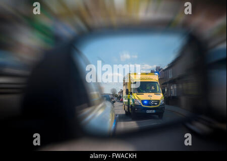 Ein Rennsport-Krankenwagen mit Blaulicht überholt ein Auto, das es in seiner Flügel Spiegel sieht Stockfoto