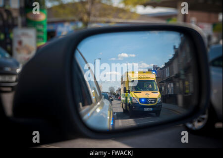 Ein Rennsport-Krankenwagen mit Blaulicht überholt ein Auto, das es in seiner Flügel Spiegel sieht Stockfoto